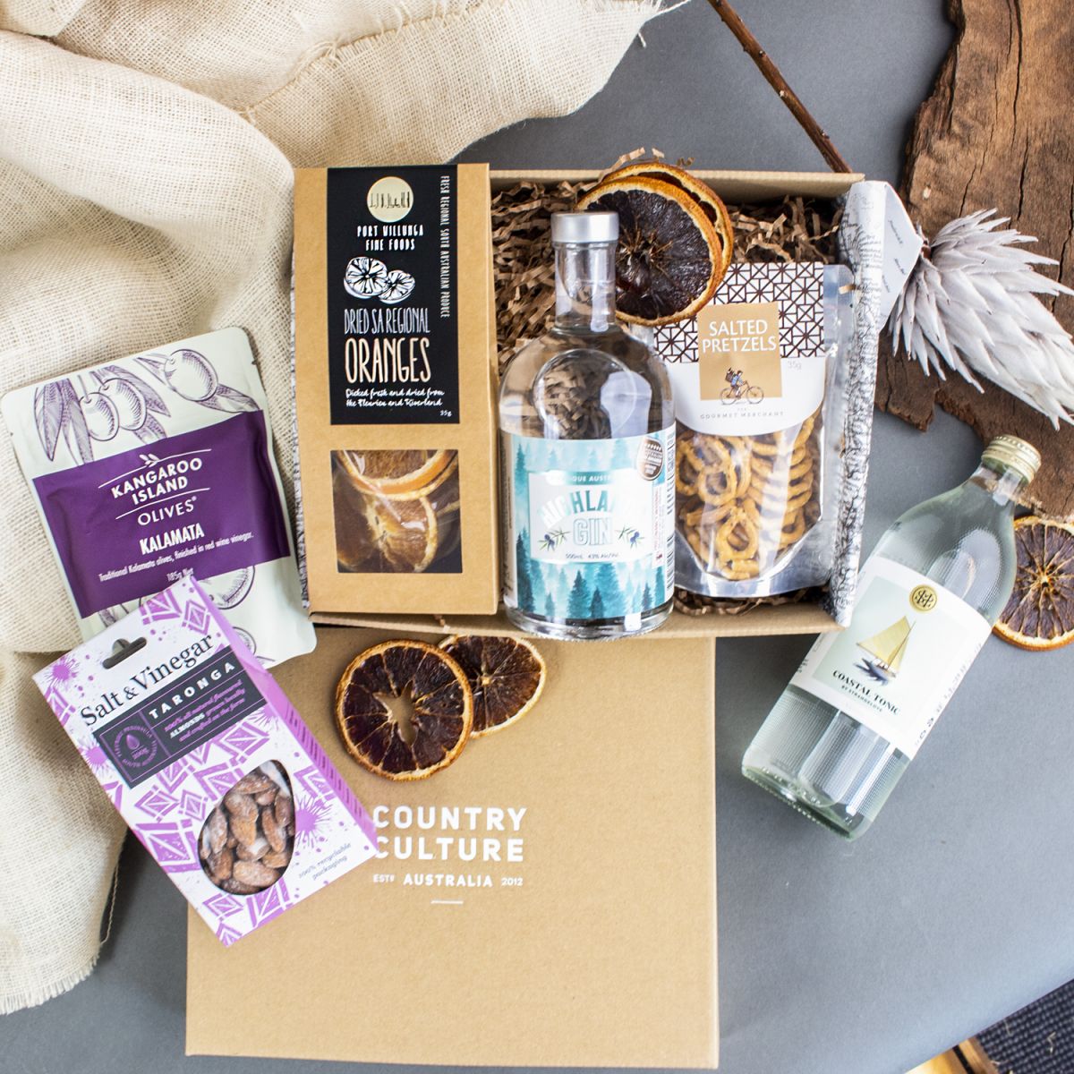 Photo of our gin and tonic cocktail kit inside an eco friendly gift box. Featuring Highlands Gin from Glen Gowrie Distillery, Dried Oranges, Salted Pretzels and Kalamata Olives.